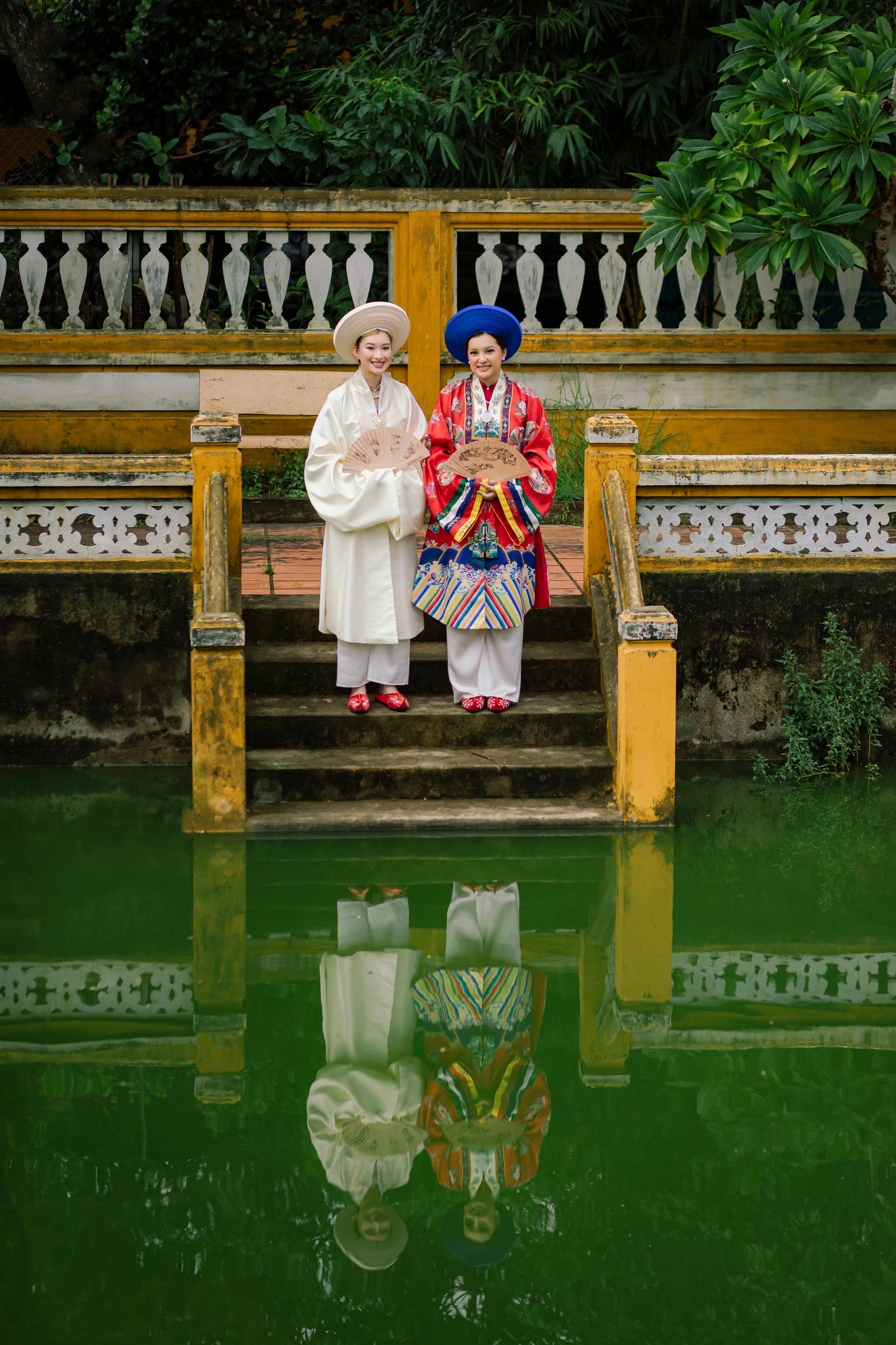 Two people in traditional Vietnamese attire standing by a serene pond in Hội An, Vietnam.