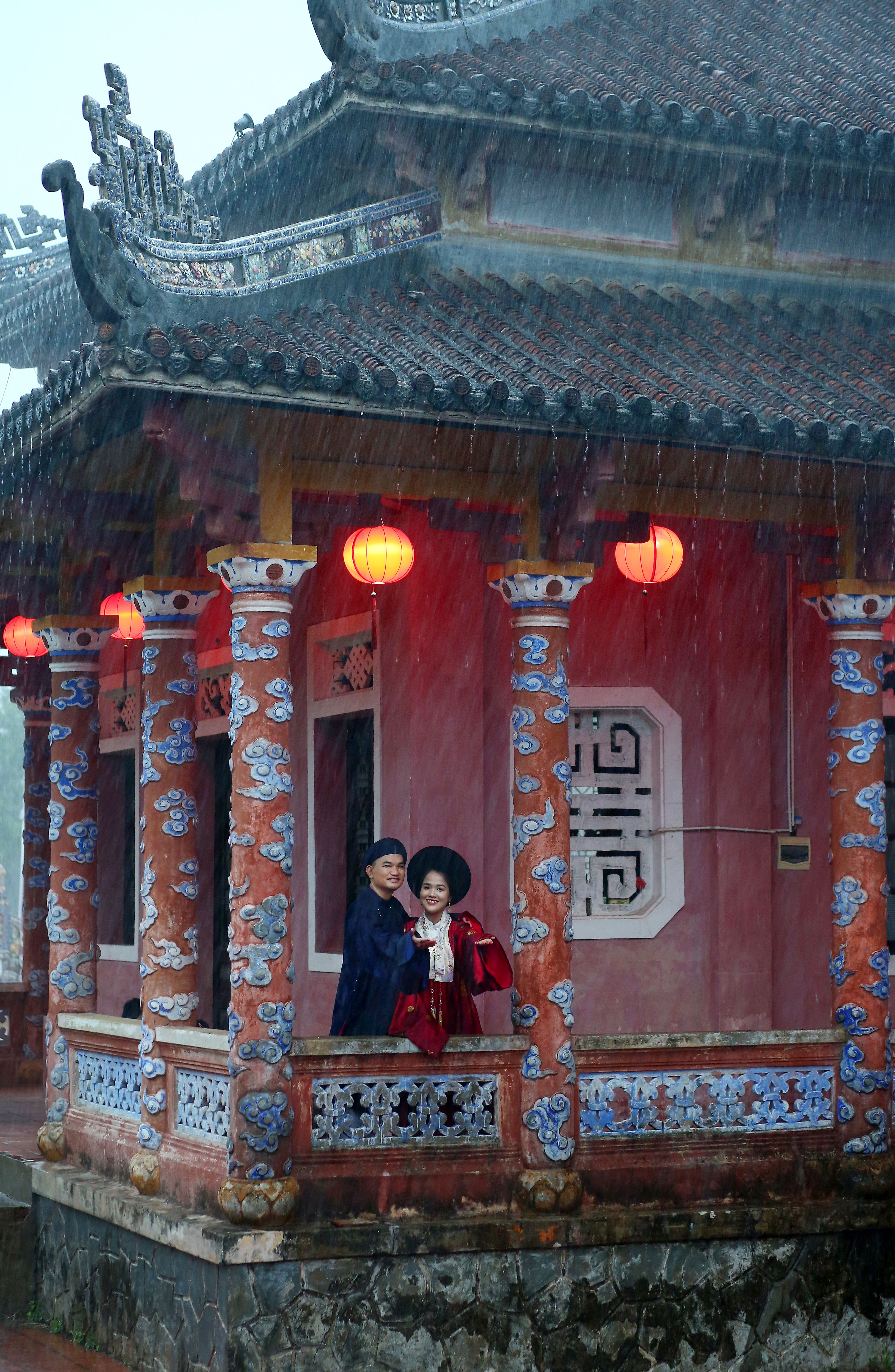 Couple in traditional Vietnamese attire standing at an ornate Hoi An building.
