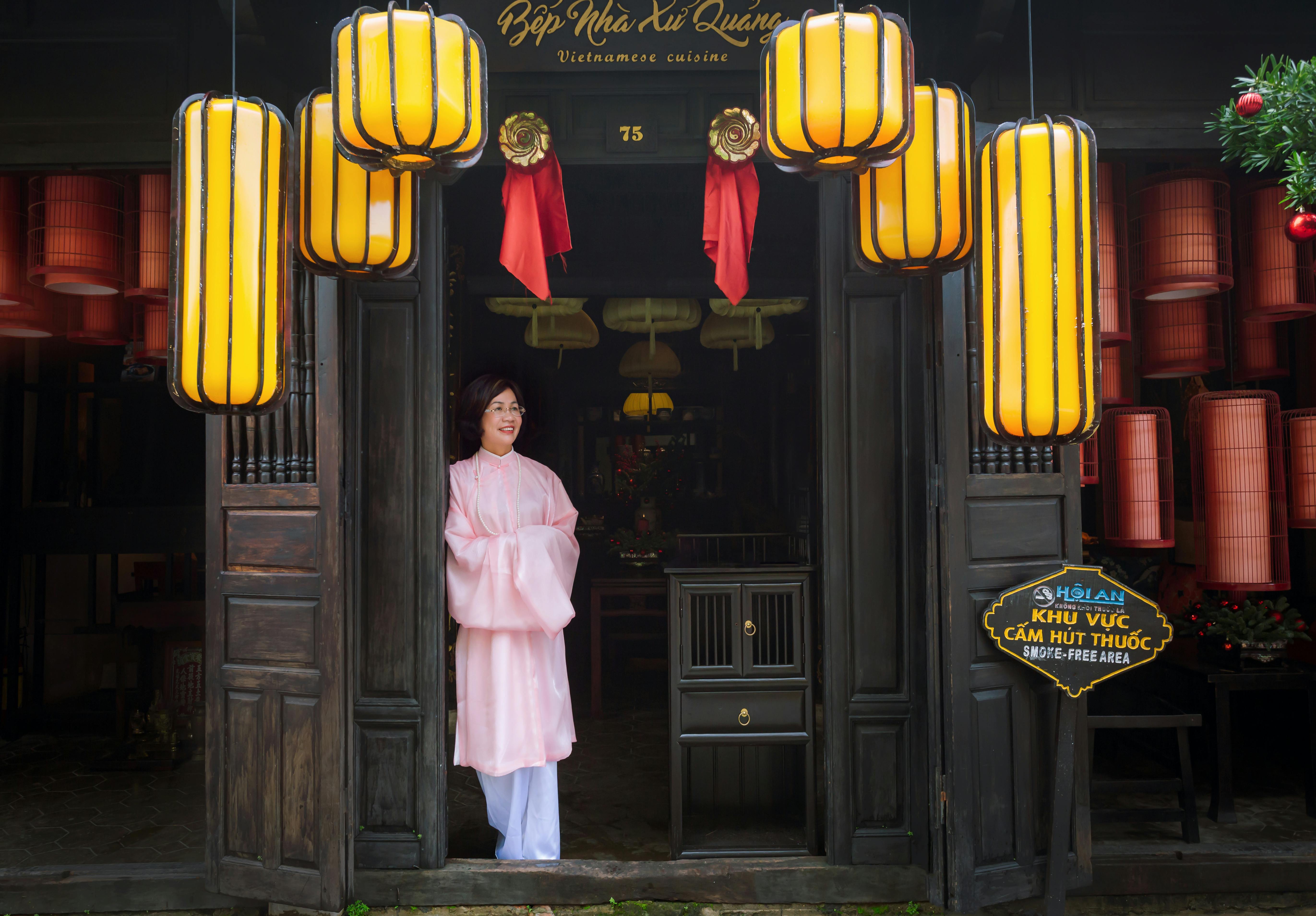 Traditional Vietnamese restaurant entrance with hanging lanterns and a woman in a long dress in Hội An.