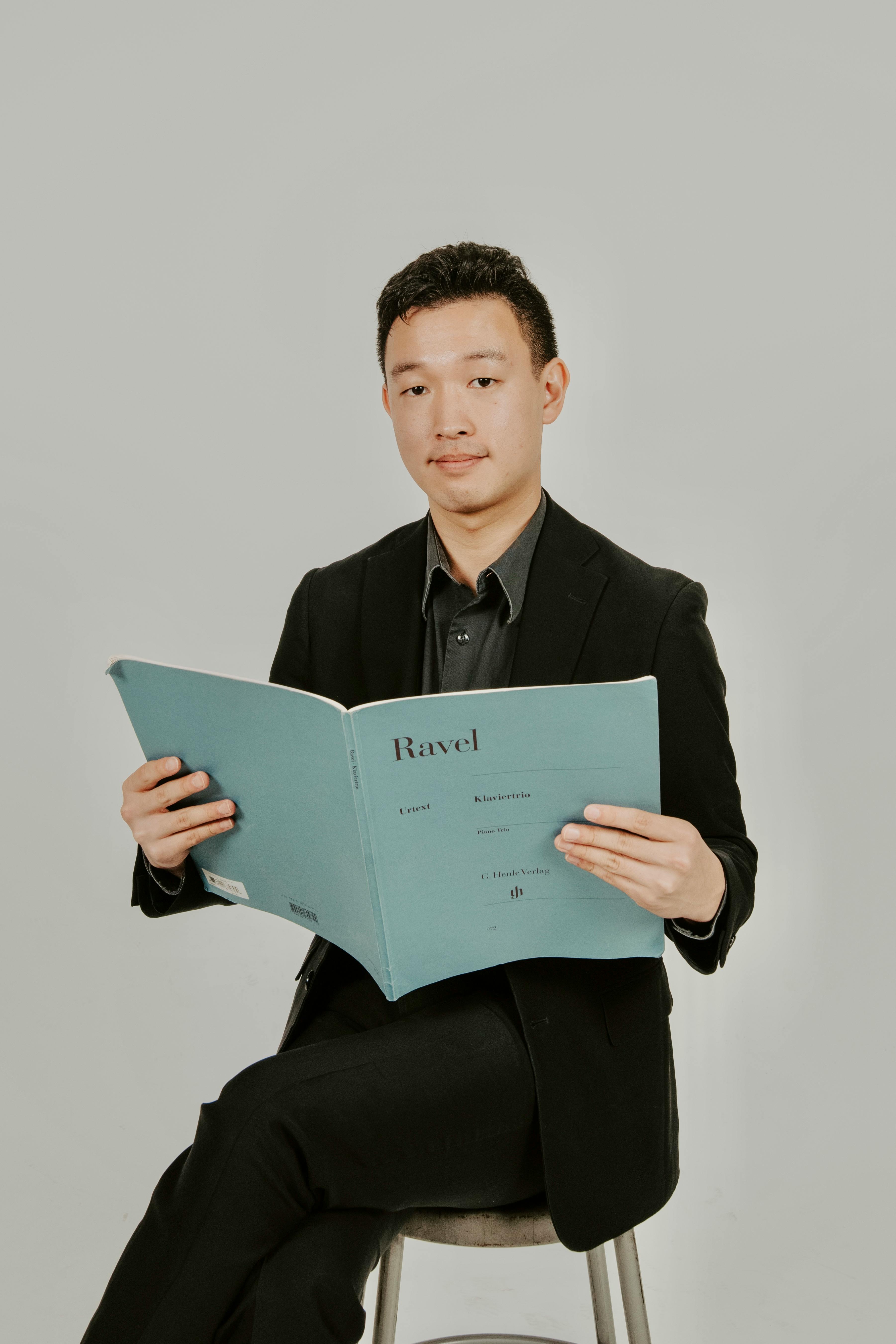 De franc Jove amb vestit fosc sostenint una partitura de Ravel sobre un fons neutre. Foto d'estoc