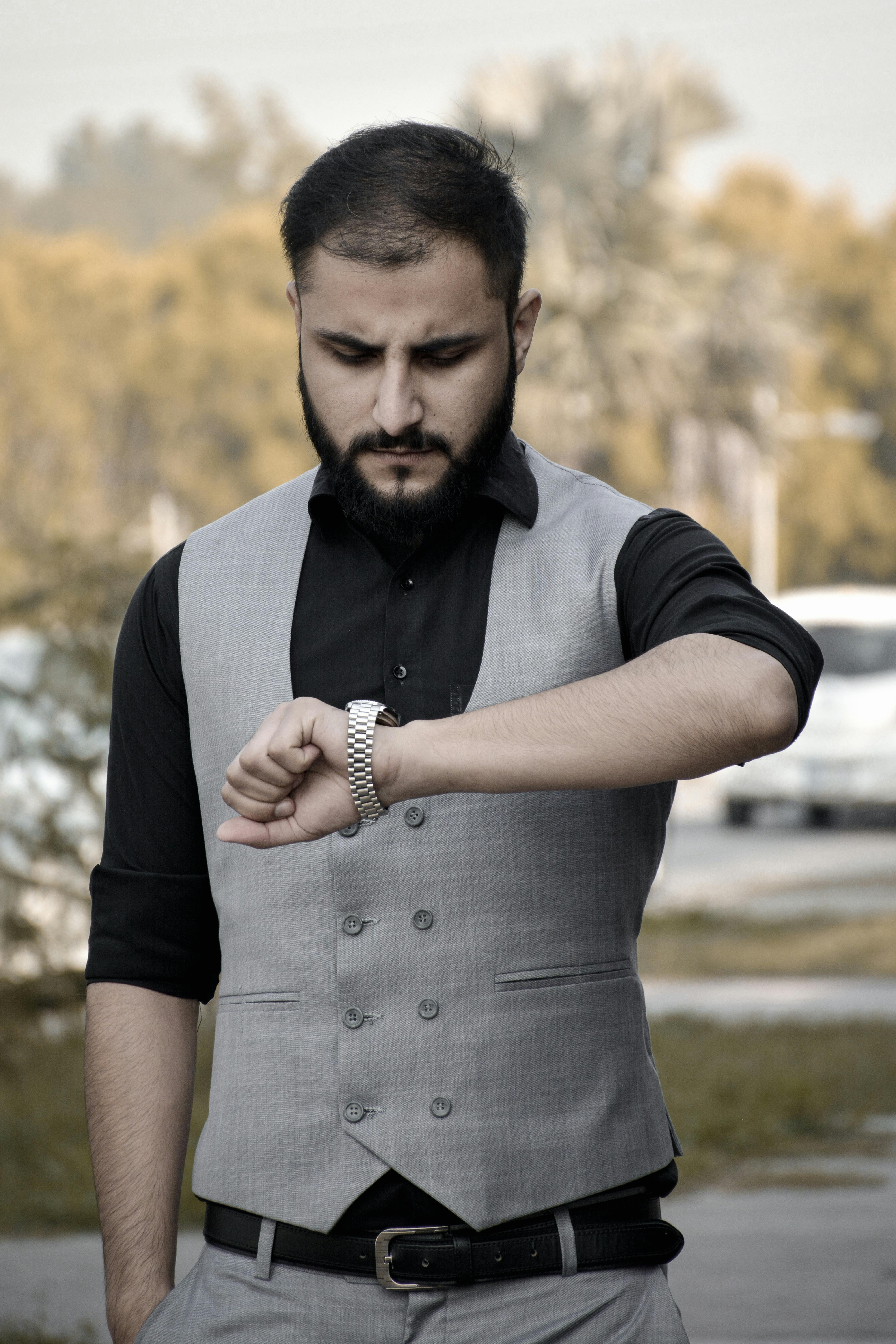 man in stylish grey vest checking time outdoors