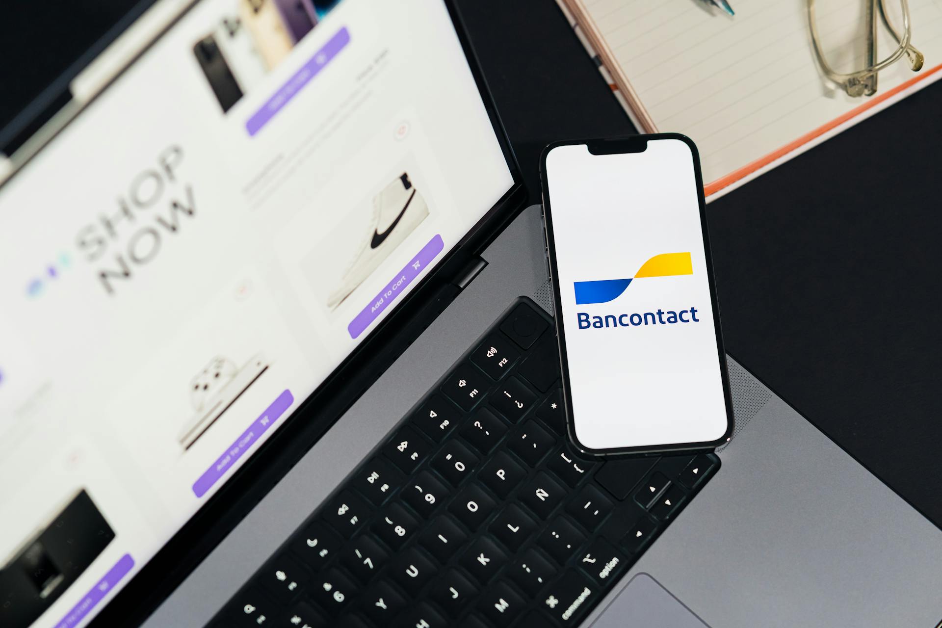 Smartphone displaying Bancontact app on laptop during online shopping.