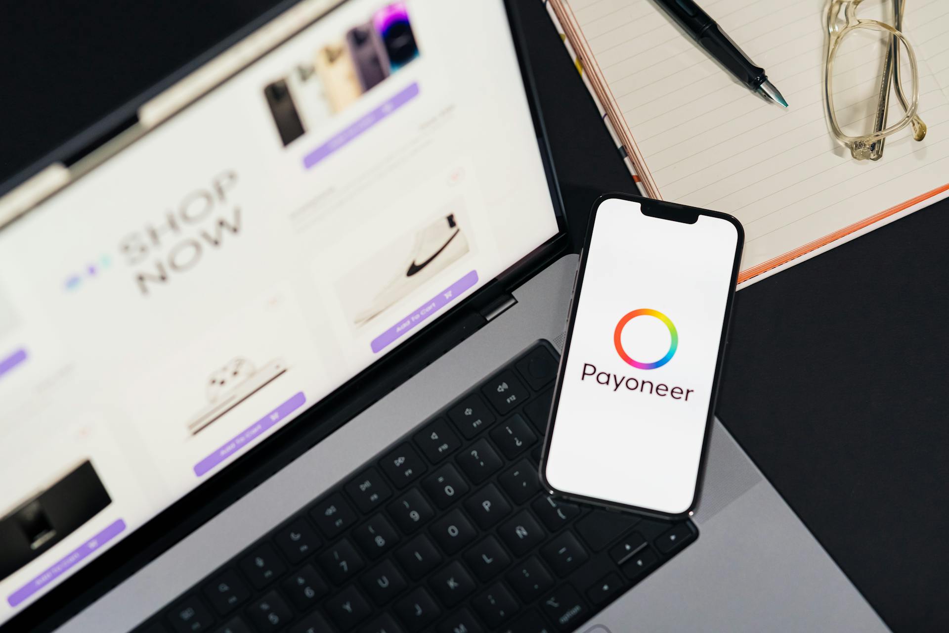 Mobile phone with Payoneer app on screen next to laptop displaying online shopping site.