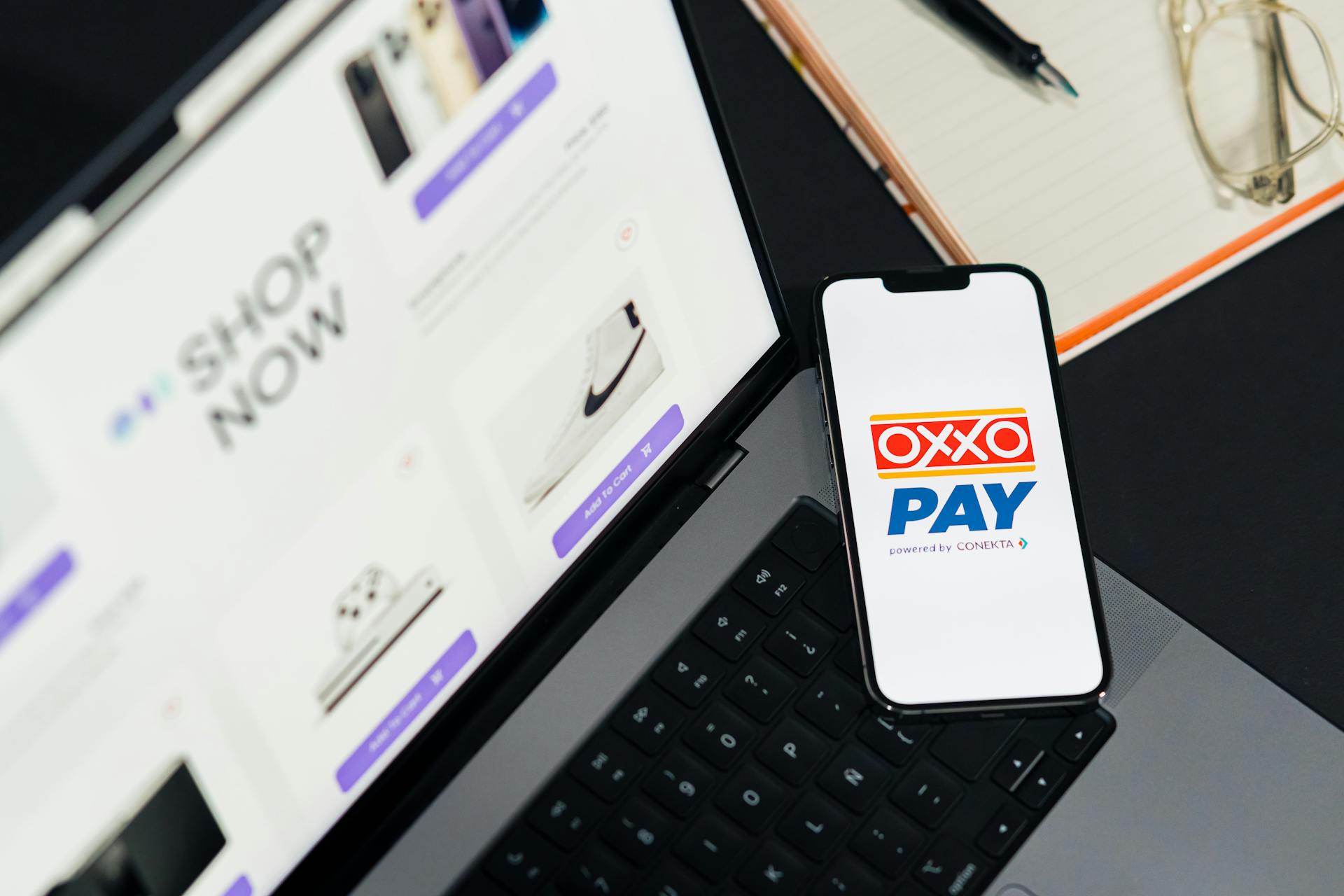 A mobile phone with OXXO Pay on a laptop used for online shopping.