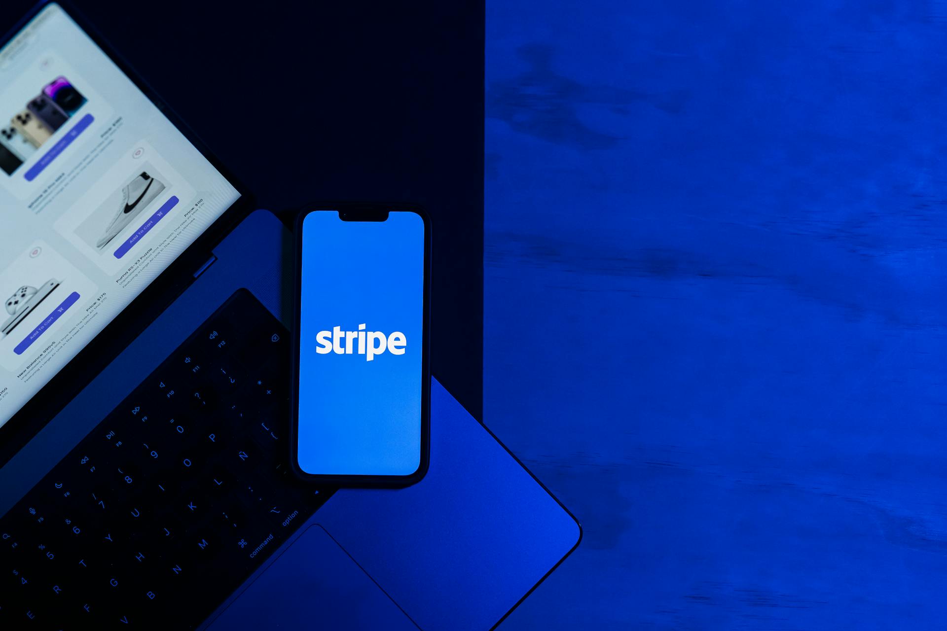 A smartphone displaying the Stripe app placed on a laptop keyboard with a blue monochromatic tone.