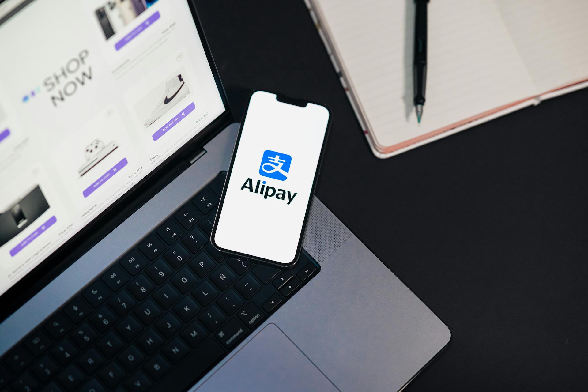 Smartphone displaying Alipay app on open laptop with online shopping site.