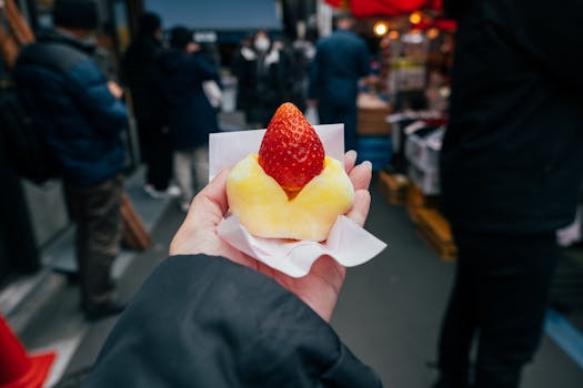 Hand holding a fruit-filled mochi in vibrant Tokyo street market setting.