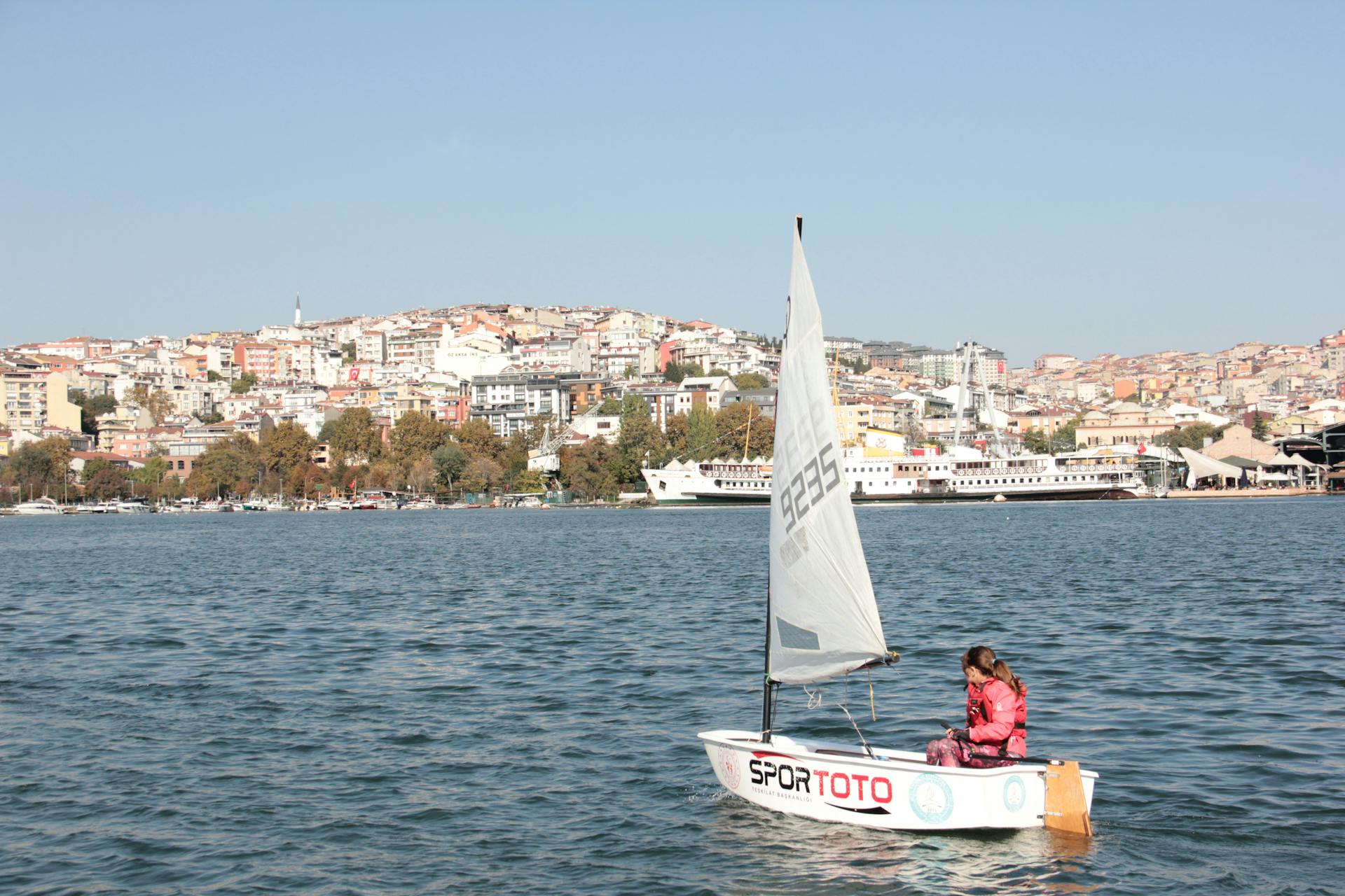 A child sails a small boat on the Golden Horn in Istanbul, showcasing a picturesque cityscape.