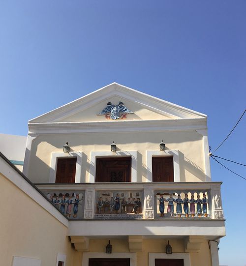 Free Neoclassical building with artistic balcony frescoes against a bright blue sky. Stock Photo