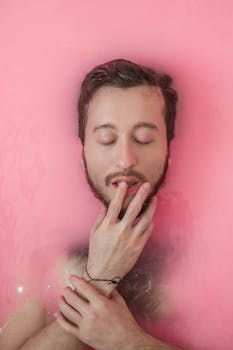 一名男子闭着眼睛，在粉红色的水中平静地沐浴