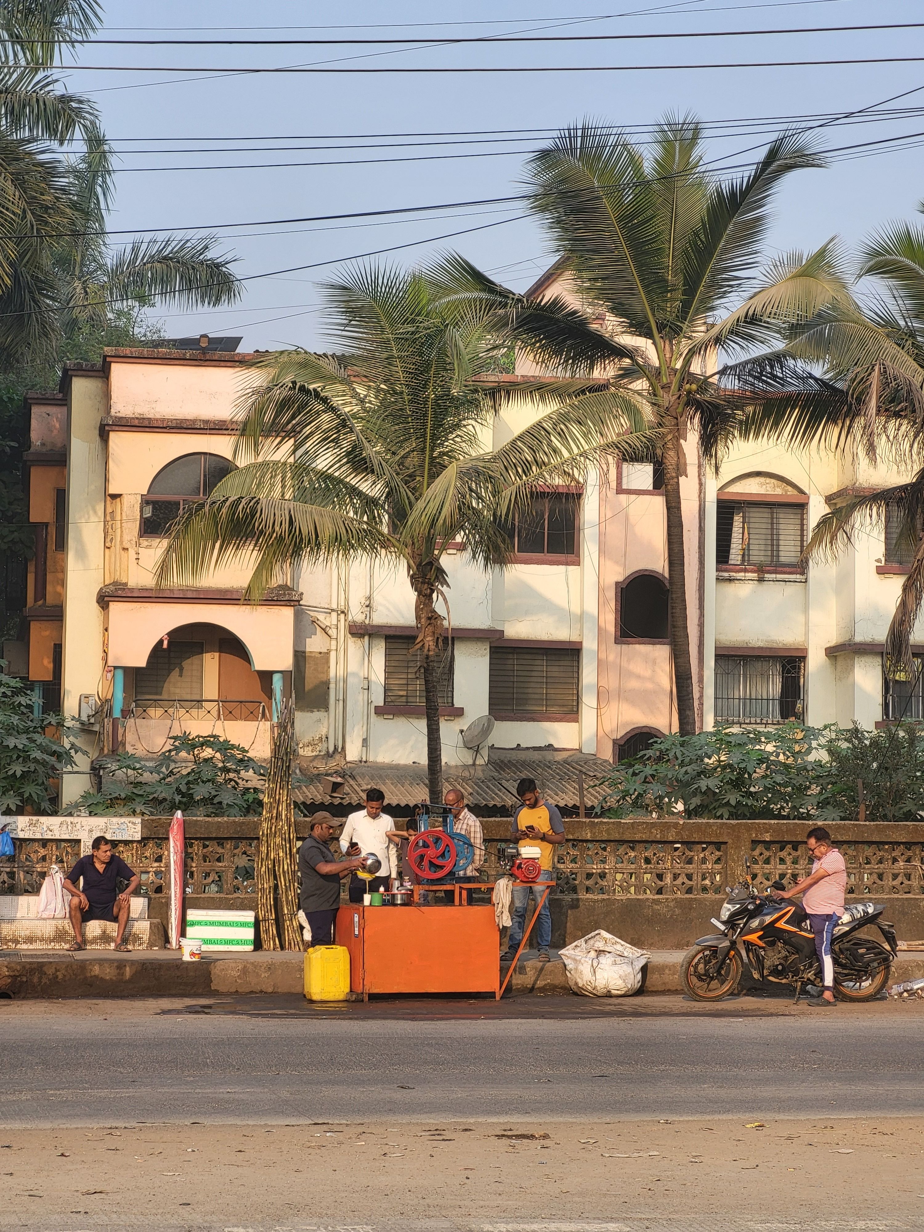 Street vendors with goods and motorbike in front of building.