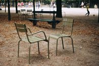 Two empty green chairs in an autumn park in Paris with blurred people in the background.