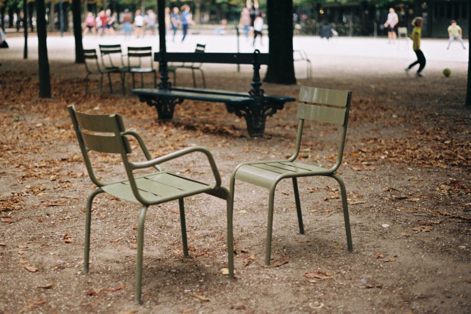 Two empty green chairs in an autumn park in Paris with blurred people in the background.