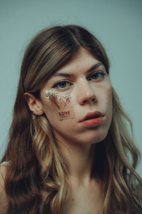 Free Portrait of a woman with the word 'Love' and flowers on her face, expressing emotion. Stock Photo
