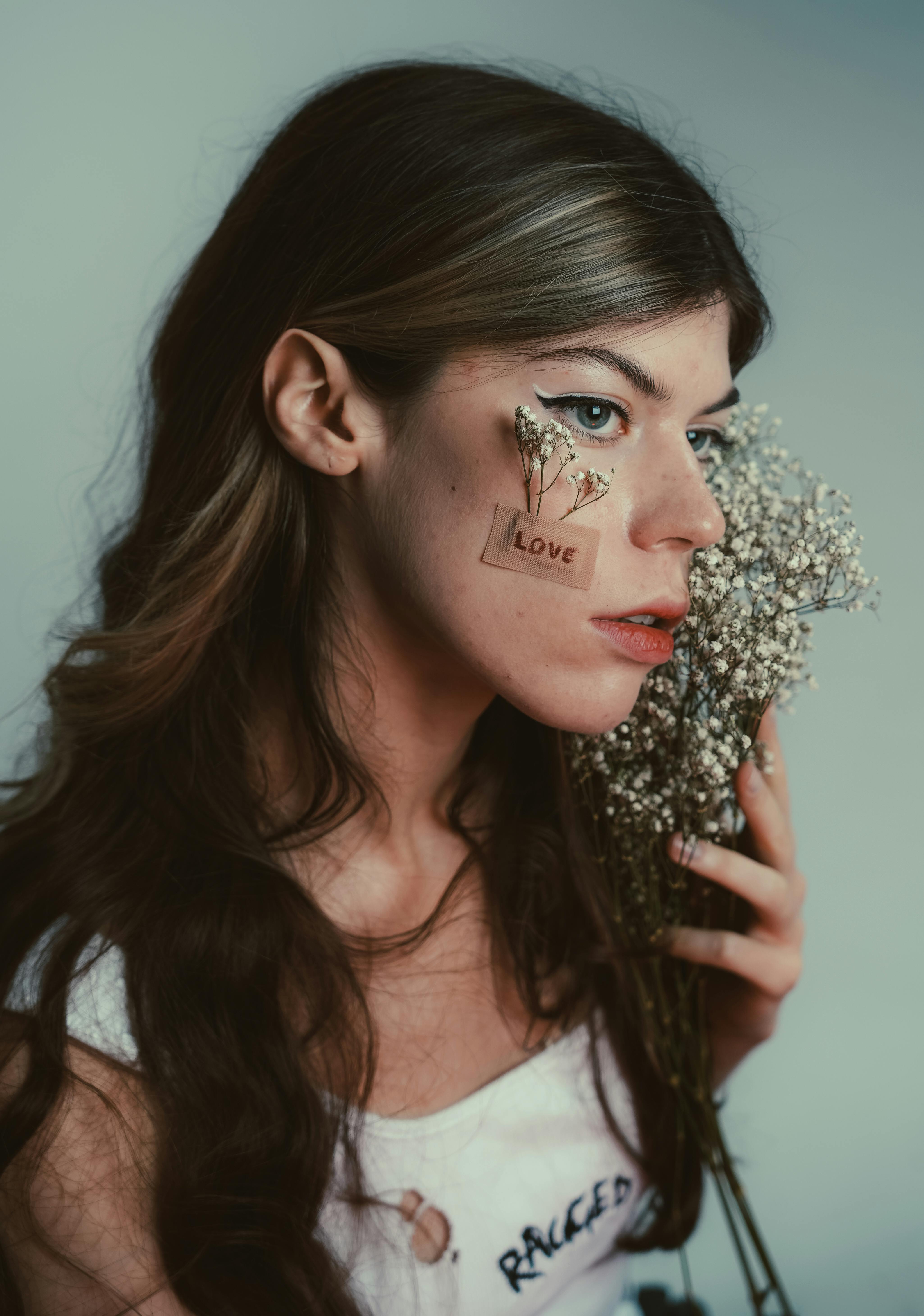 Portrait of a woman holding flowers with a love message on her cheek.