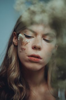 Close-up of a woman with floral face tattoo and 'love' inscription, expressive and thoughtful.