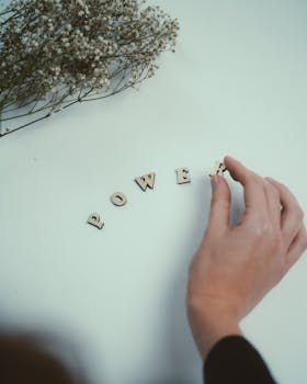A person arranges wooden letters to spell 'power' with delicate flowers nearby.
