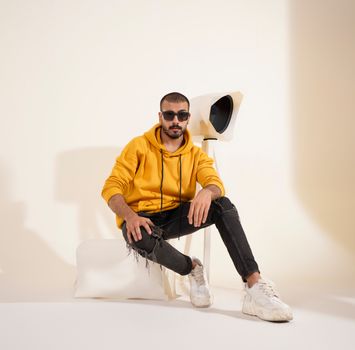 Fashionable male model in a trendy yellow hoodie and sunglasses posing indoors with contemporary lighting.