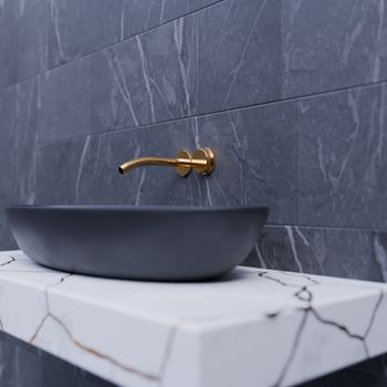 Elegant bathroom sink with gold faucet on marble slab and gray tiles.