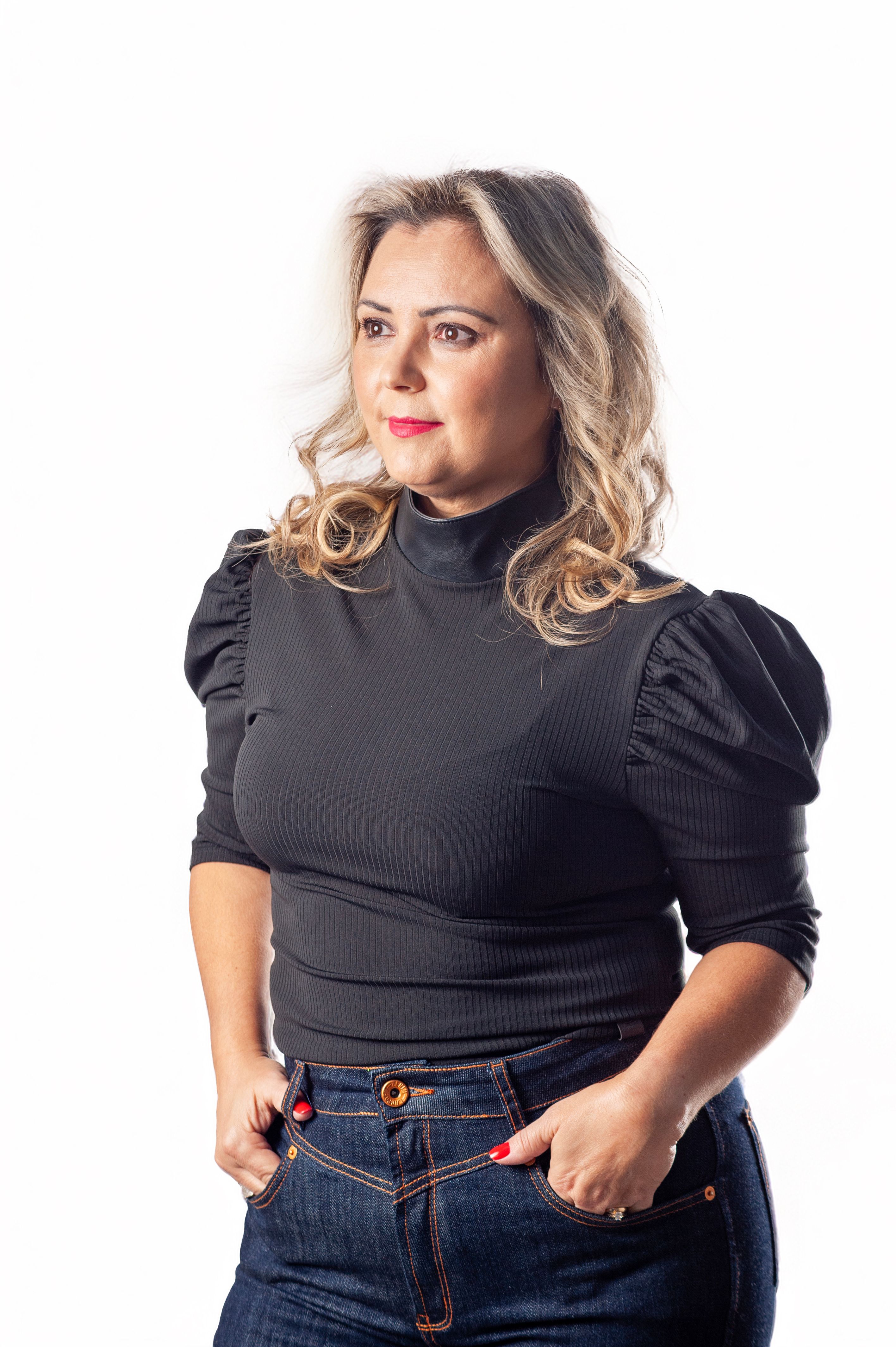 Elegant portrait of a woman in a black top and denim jeans against a white background.
