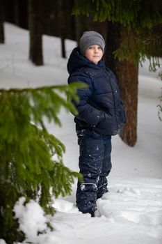 A young child in a snowy forest dressed in winter gear, standing by trees.