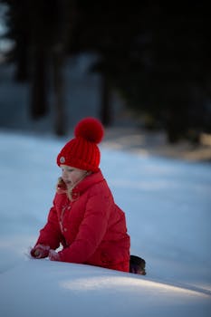 Young girl in a red coat and hat enjoying the snow outdoors during winter.