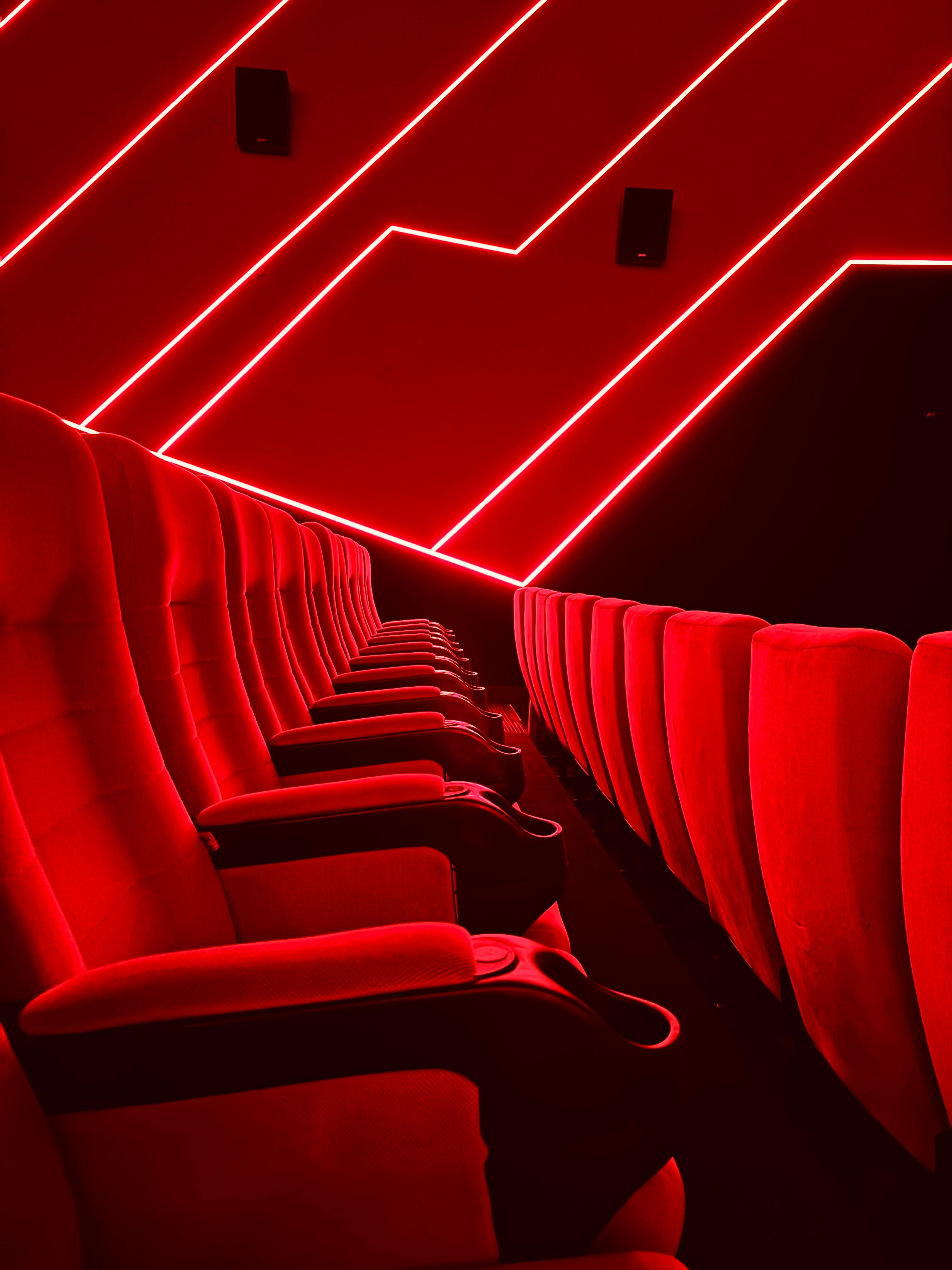 Ücretsiz Kırmızı neon ışıklarla aydınlatılmış canlı tiyatro koltukları, modern bir sinema iç mekanı sergiliyor. Stok Fotoğraflar