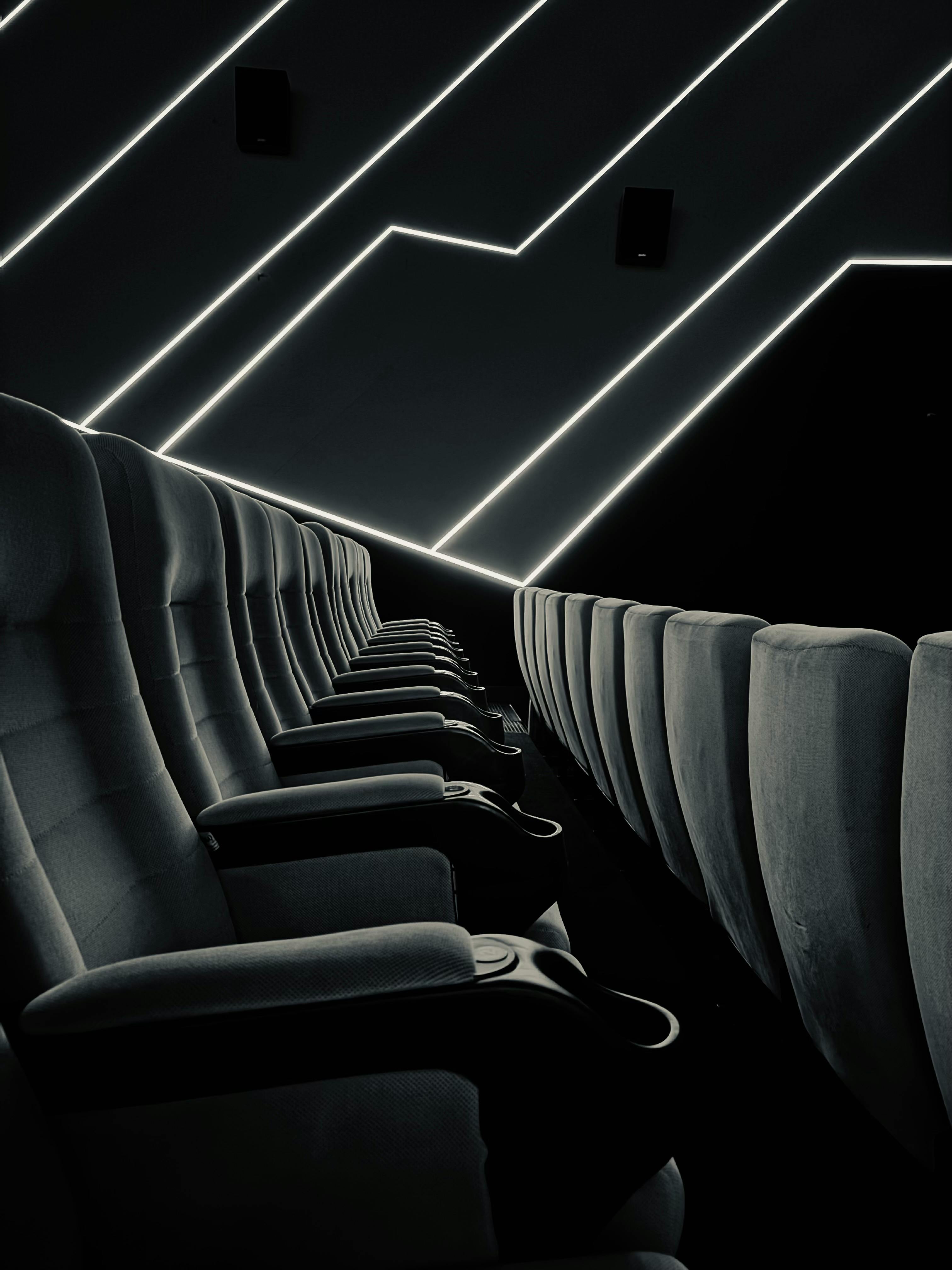 Gratuit Salle de cinéma sombre avec des rangées vides de sièges noirs et des lignes d'éclairage ambiant. Photos