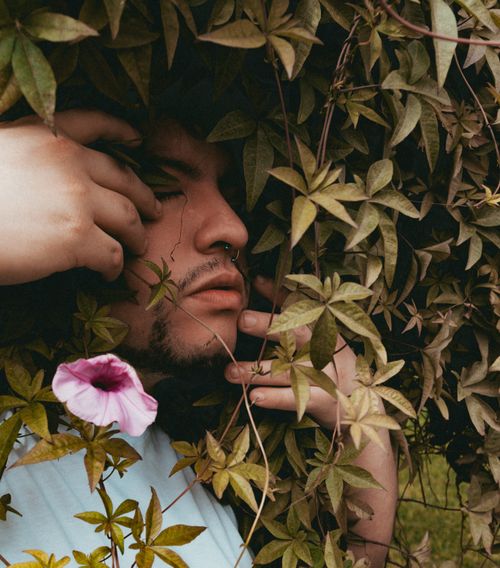 Free Man surrounded by vibrant greenery and flower, eyes closed in peaceful nature embrace. Stock Photo