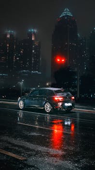 A sleek car on a wet city street reflecting tower lights at night.