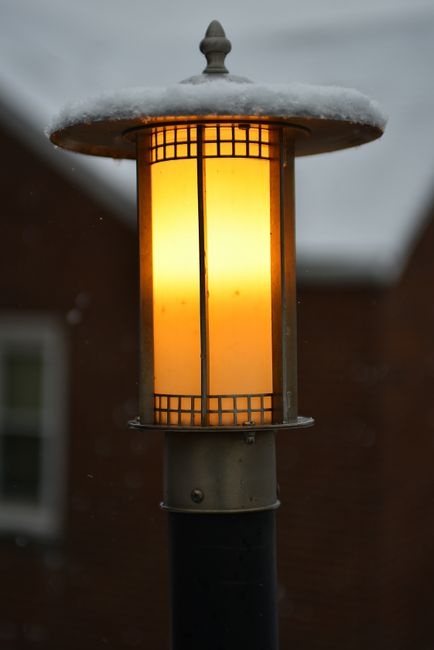 A warm glowing lamp post dusted with snow, set against a wintery backdrop.