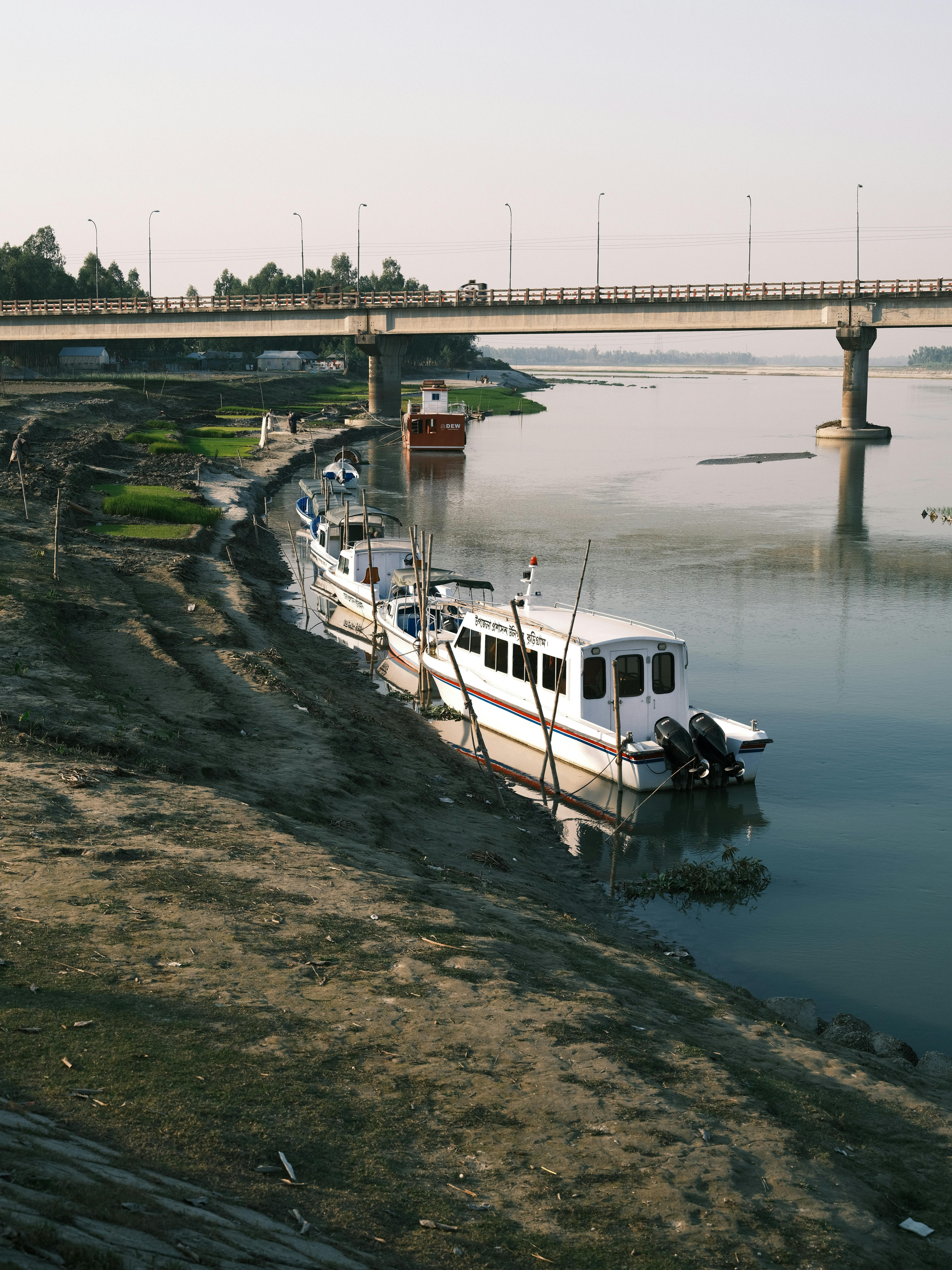 Boats docked along a calm river under an urban bridge during the day.