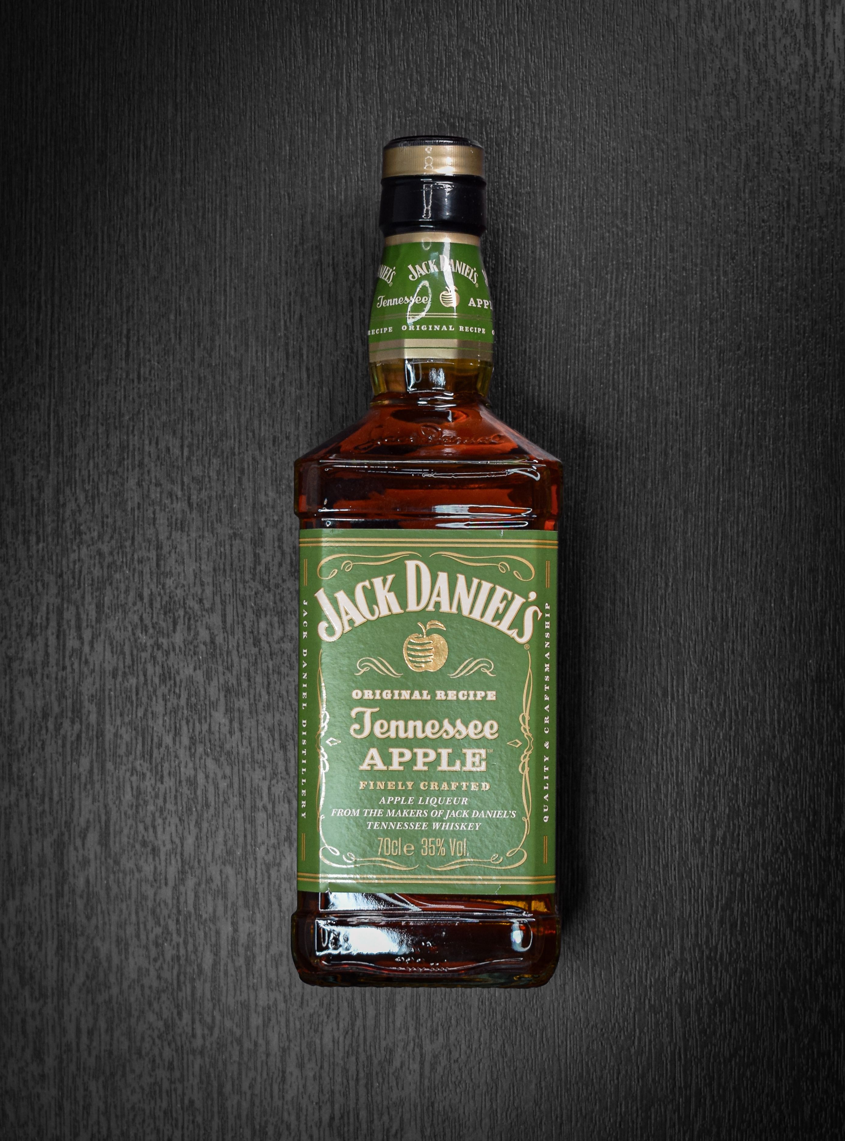 Bottle of Jack Daniel's Tennessee Apple whiskey displayed on a dark wooden background for product photography.