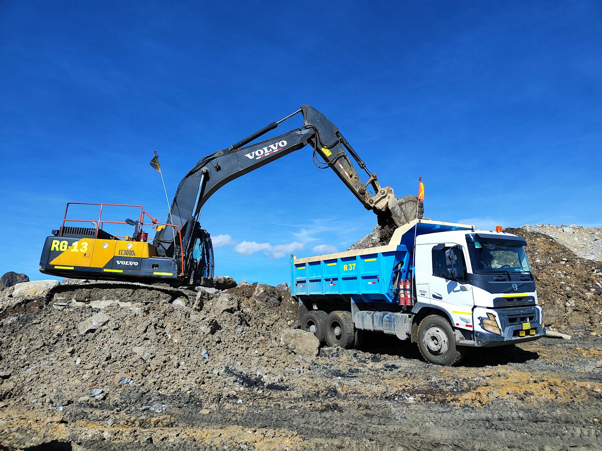 Excavator loading soil onto truck on a sunny day at a construction site.