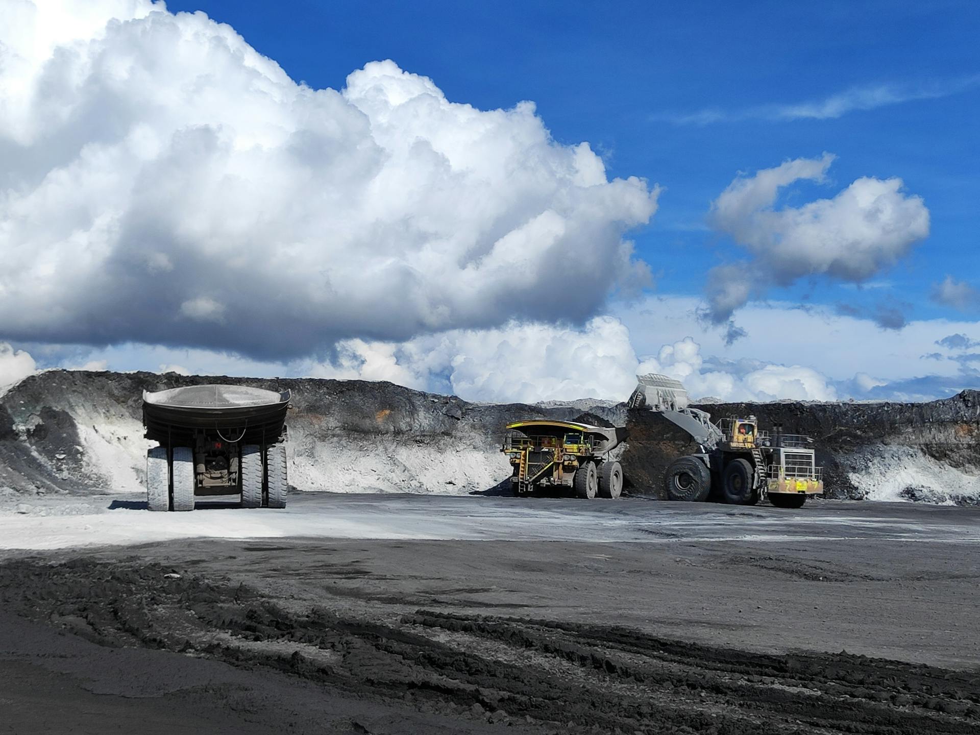 Open-pit mine with large trucks and excavators under blue sky.