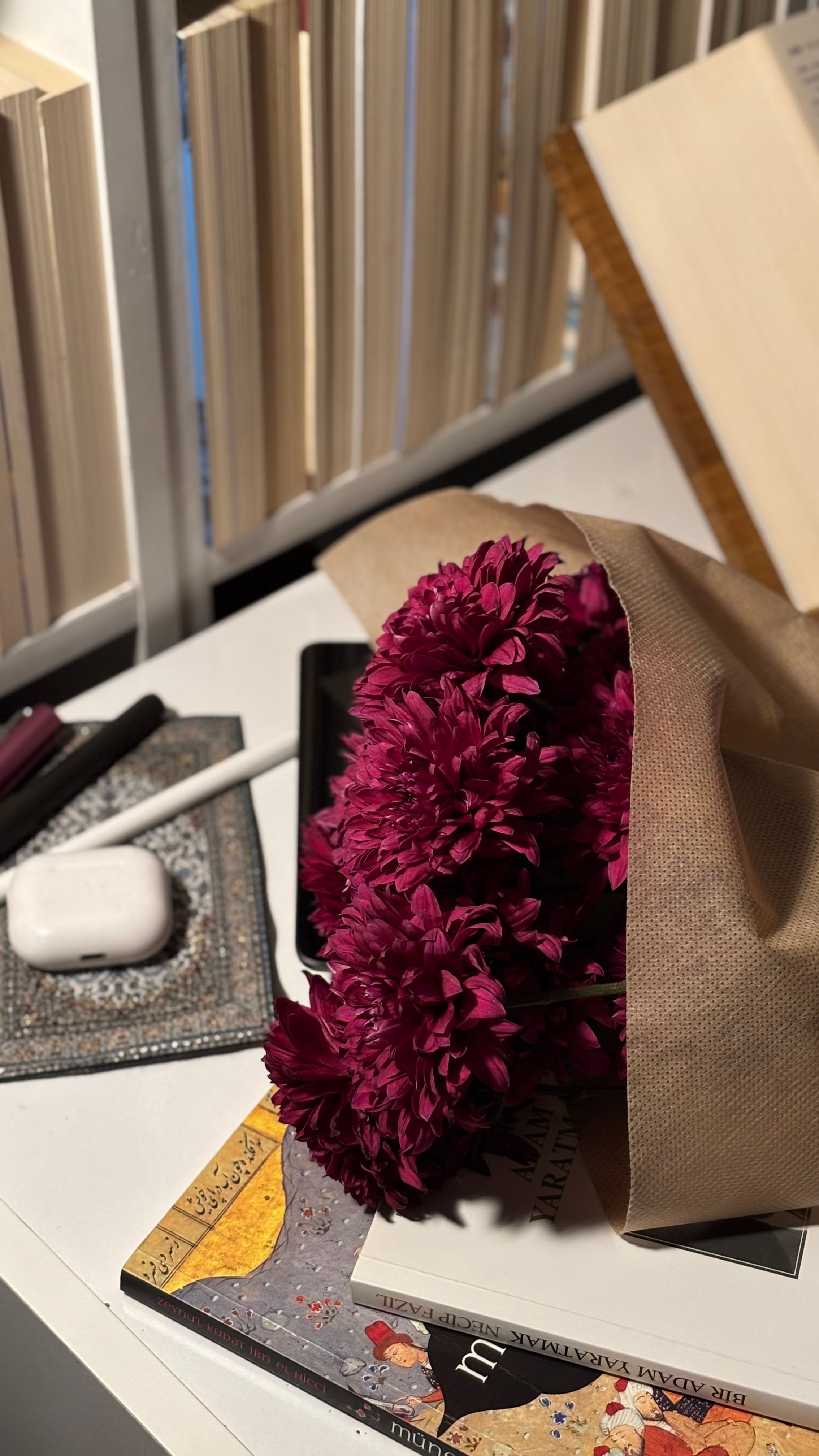 A bouquet of purple flowers on a desk surrounded by books and electronic gadgets.