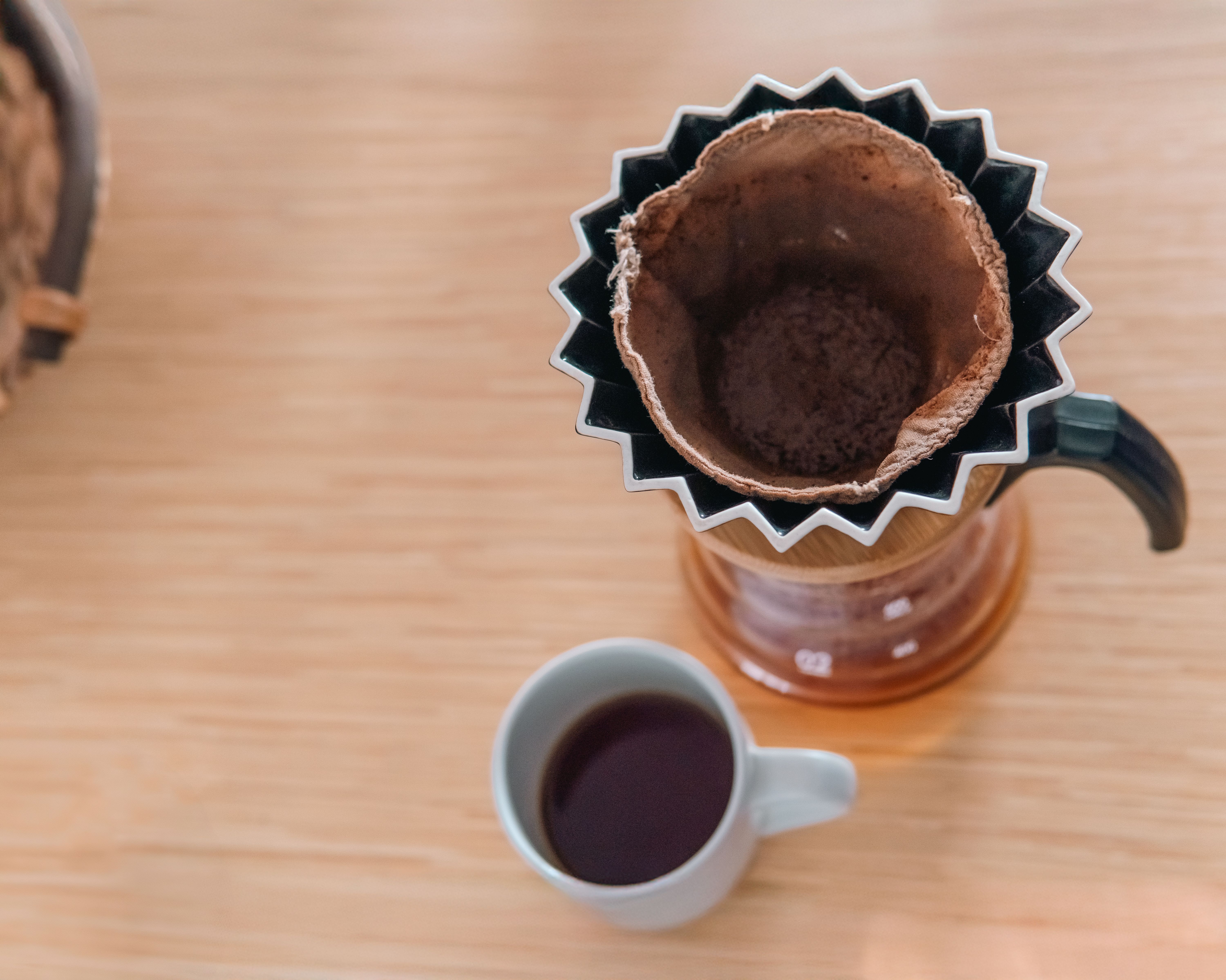 Freshly brewed coffee in a white cup on a wooden table with Bero Coffee bags in the background