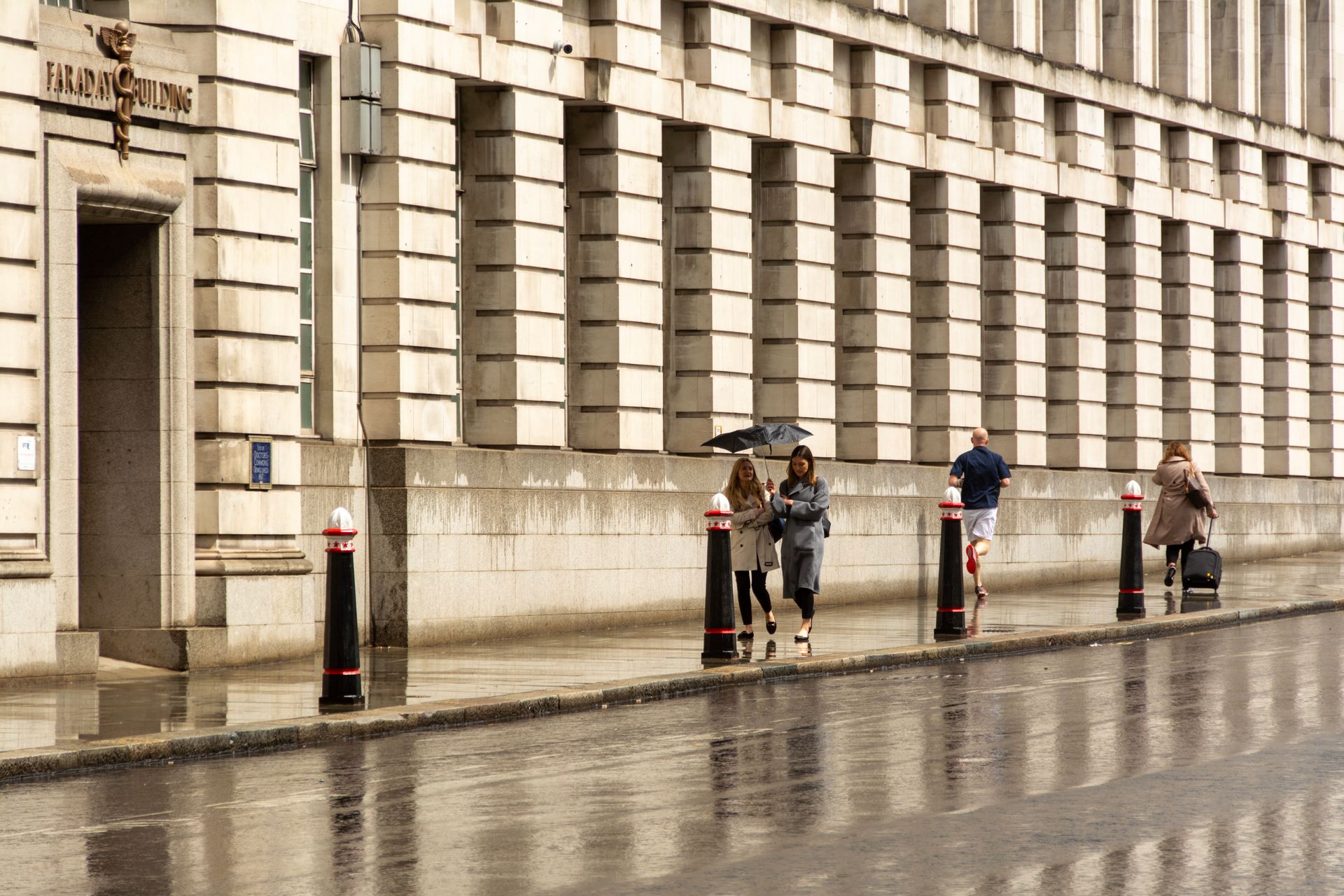 Pedestrians walk by the Faraday Building in London on a rainy day.