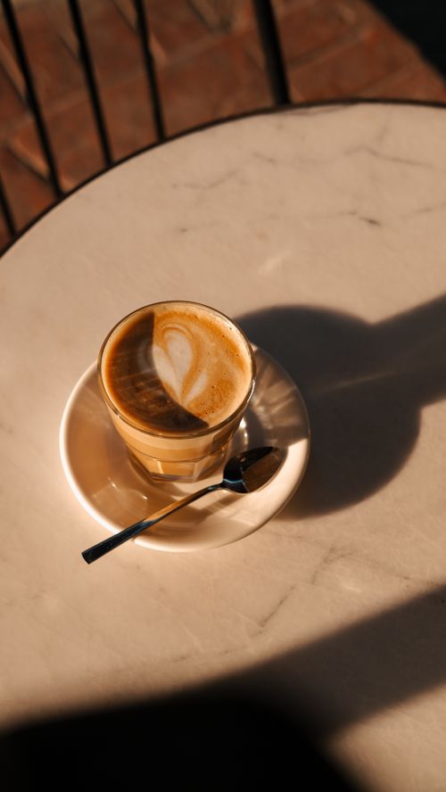 Free A captivating latte with creamy foam design on a marble table, bathed in warm sunlight. Stock Photo