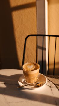 A warm sunlit latte with heart foam art on a marble table, perfect for coffee lovers.