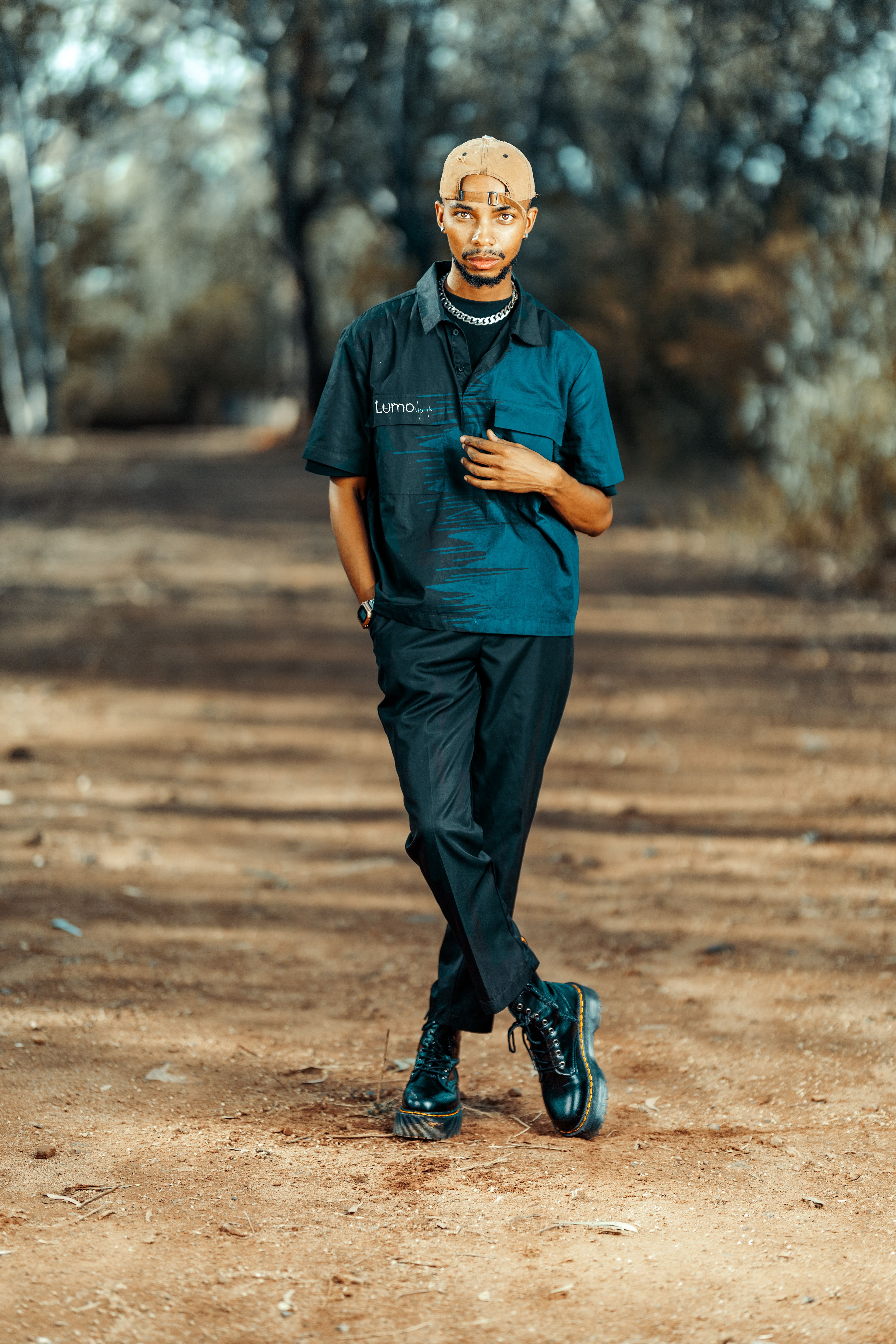 Man wearing fashionable clothes walking on a rustic outdoor path with blurry background.
