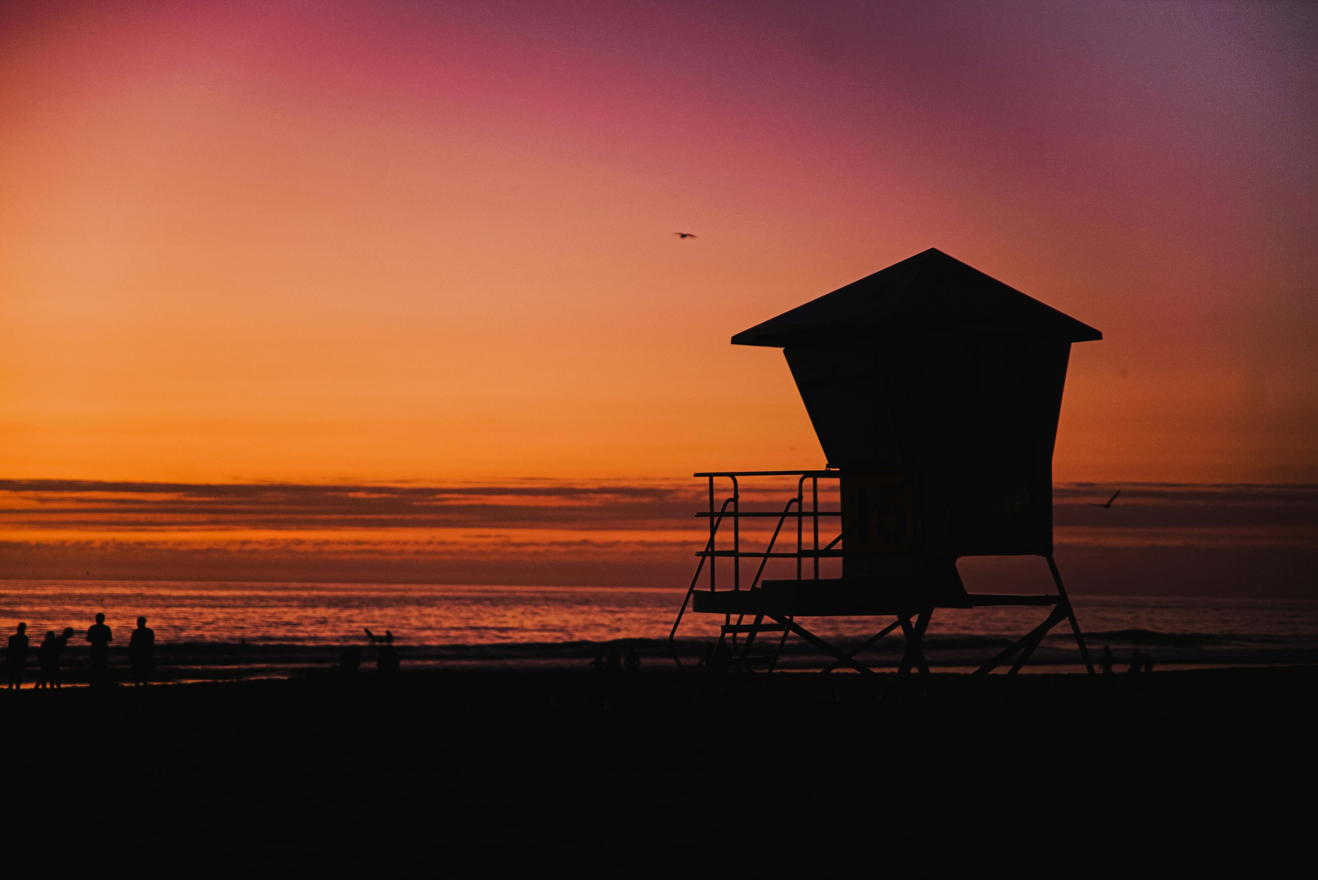 夕阳下，救生员塔的剪影映衬着人们享受海滩宁静的画面，非常适合旅行和休闲主题