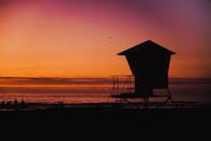 夕阳下，救生员塔的剪影映衬着人们享受海滩宁静的画面，非常适合旅行和休闲主题