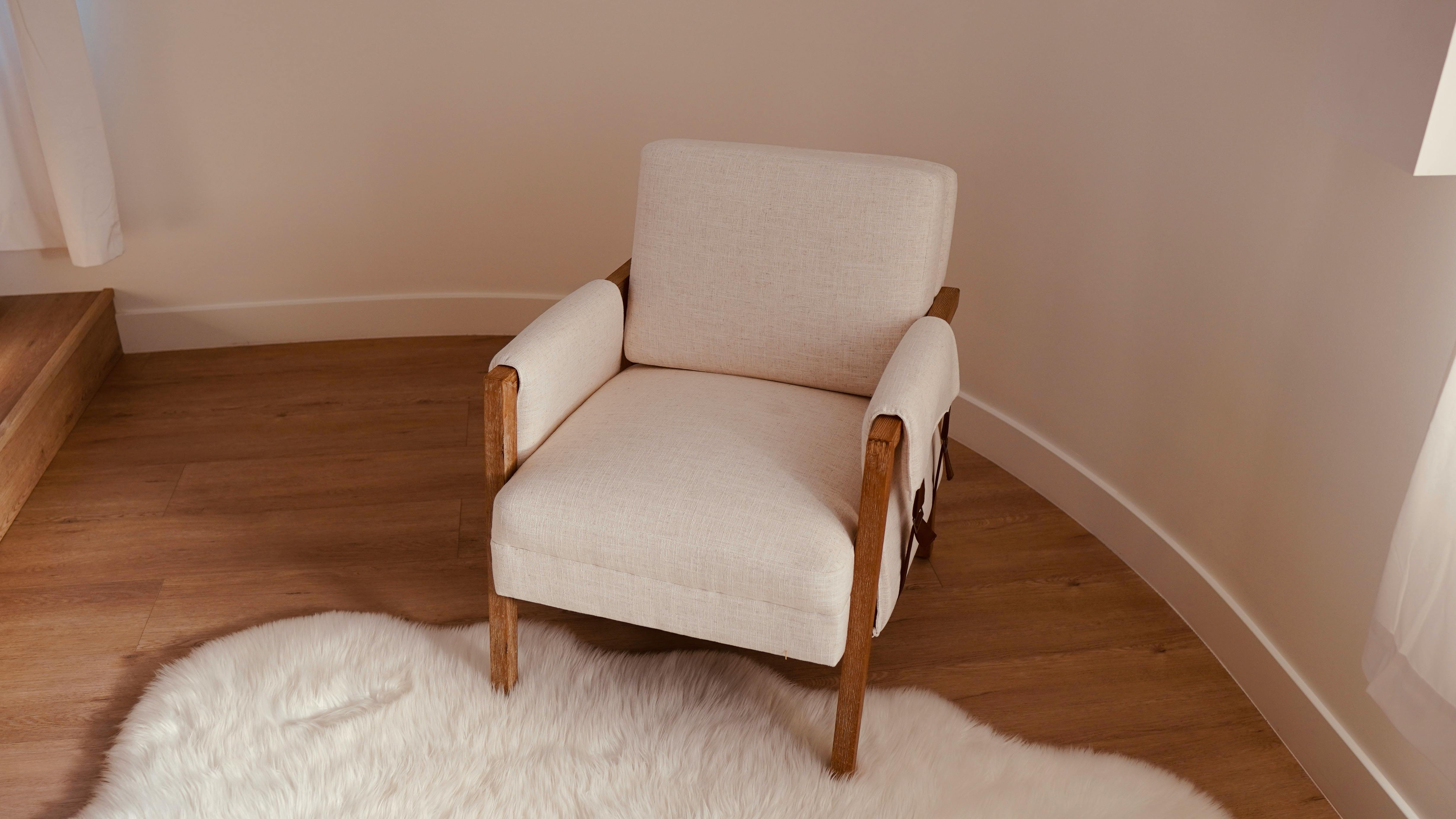 Free Elegant cream armchair in a minimalist room with wooden flooring and a soft rug. Stock Photo