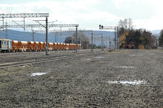 Long freight train on a gravel railway track with distant hills and clear sky.