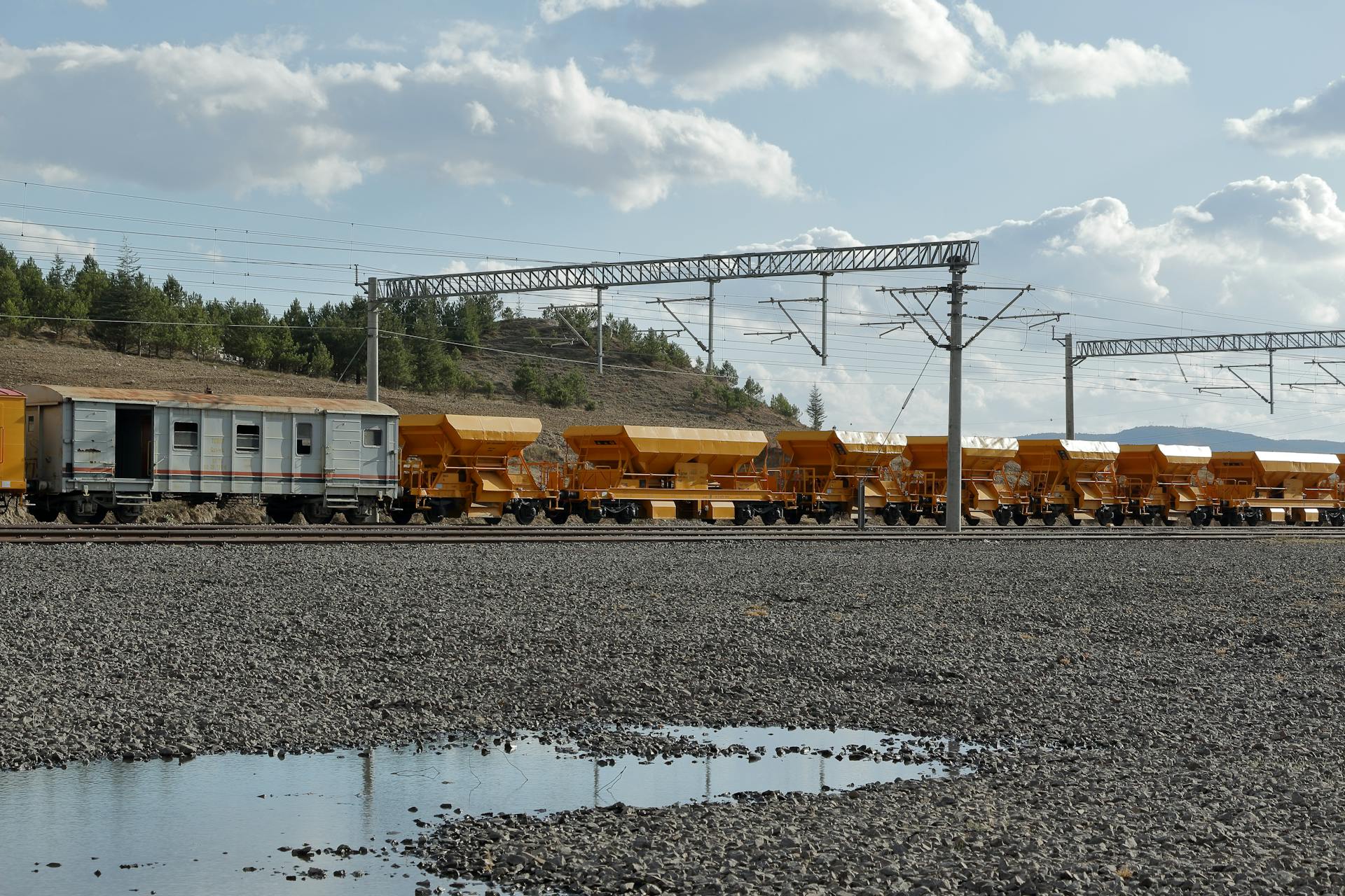 Freight train with yellow wagons on a railway track outdoors under a cloudy sky.