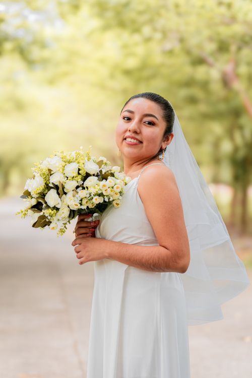 Free A smiling bride holding a white bouquet in a serene outdoor setting. Stock Photo