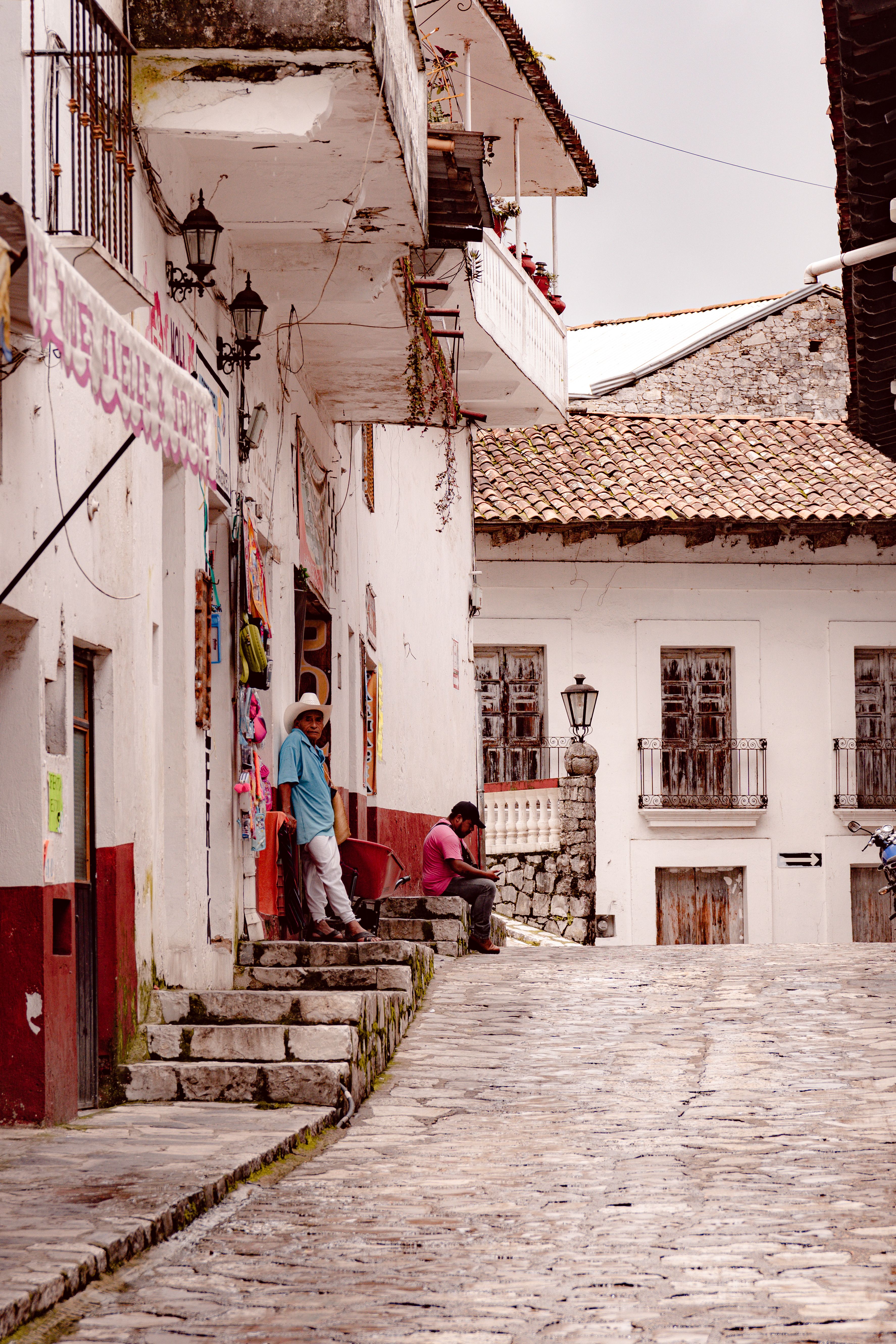 A quaint cobbled street scene in a historical town with people relaxing outdoors.