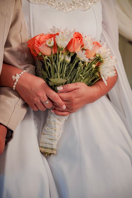Free Close-up of a bride's hands holding a peach rose and white daisy bouquet, showcasing wedding elegance. Stock Photo