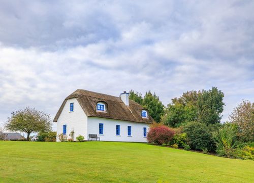 Free Scenic view of a traditional thatched cottage surrounded by lush greenery in County Clare, Ireland. Stock Photo